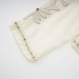 Woman wearing white pleated jacket and dress set with embellishments Blanche design matching outfit formal attire