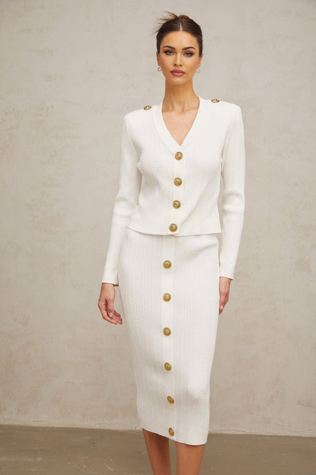 Woman wearing white ribbed knit jacket and matching skirt set standing against plain background