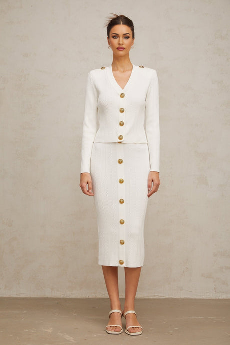 Woman wearing white ribbed knit jacket and matching skirt set standing against plain background