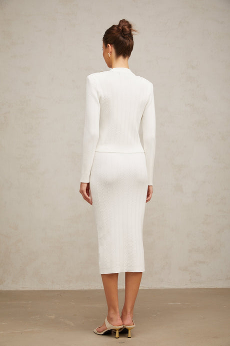 Woman wearing white ribbed knit jacket and matching skirt set standing against plain background
