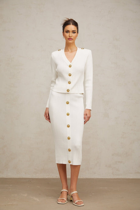 Woman wearing white ribbed knit jacket and matching skirt set standing against plain background