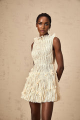 Woman wearing white semi sheer lace mini dress with crinkled texture and short sleeves standing against plain background