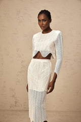 Woman wearing white twopiece outfit consisting of wavy woven top and matching skirt standing against neutral background