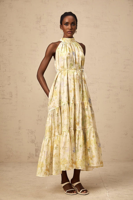Woman wearing yellow sleeveless midi dress with floral print pattern standing against plain background