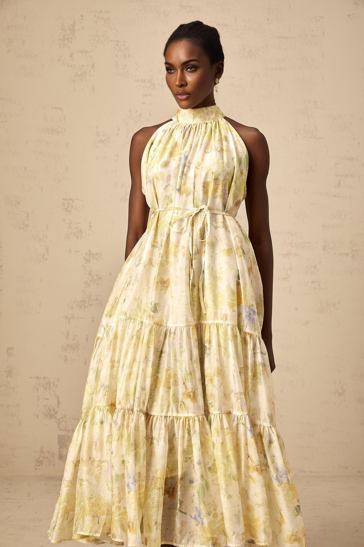 Woman wearing yellow sleeveless midi dress with floral print pattern standing against plain background