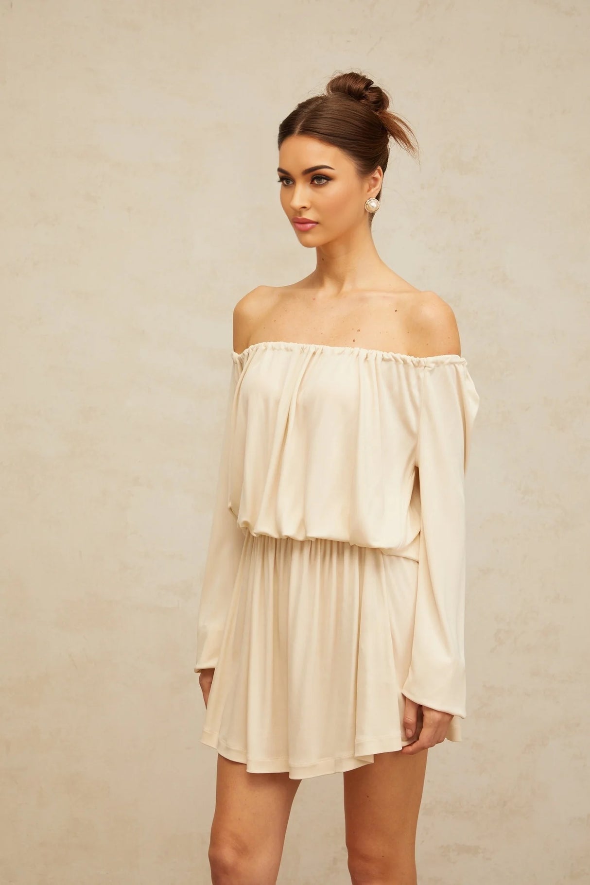Young woman wearing a beige mini dress with structured design details standing against a neutral background