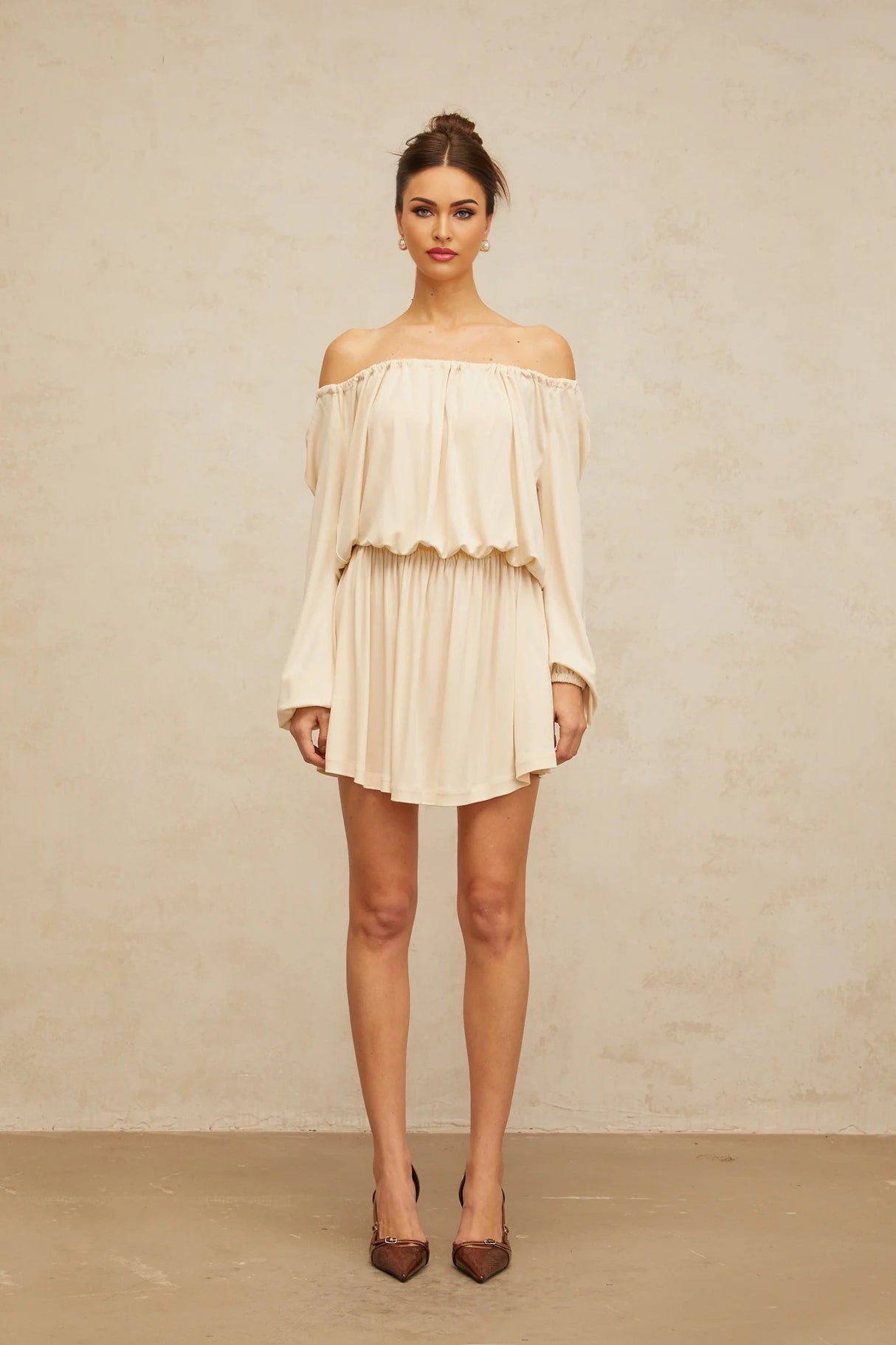 Young woman wearing a beige mini dress with structured design details standing against a plain background