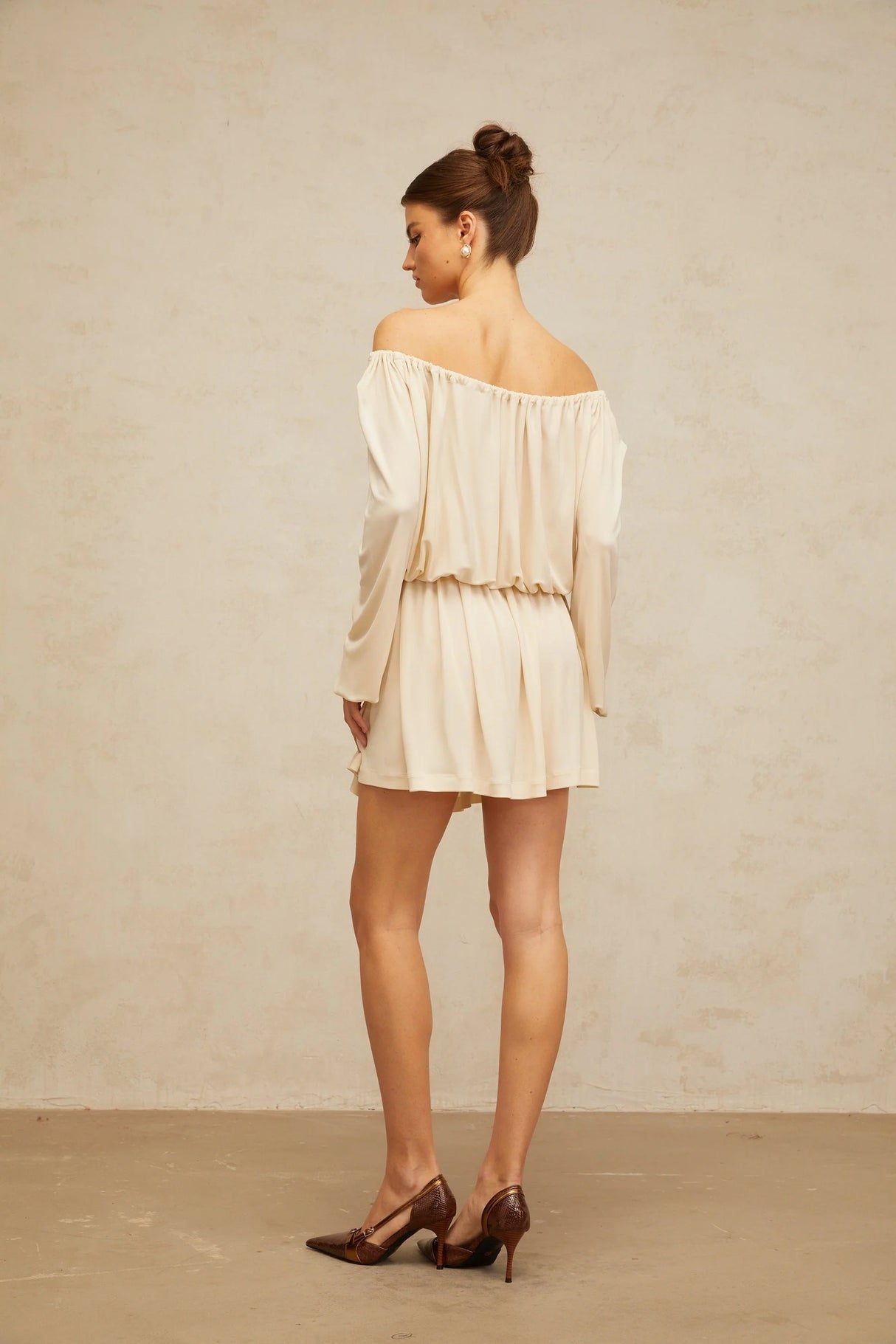 Young woman wearing a beige mini dress with structured design standing against neutral background