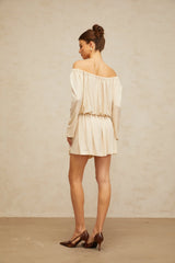 Young woman wearing a beige mini dress with structured design standing against neutral background