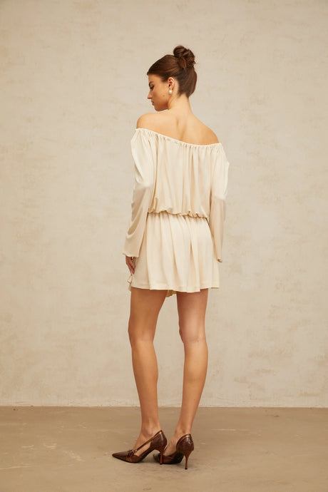 Young woman wearing a beige mini dress with structured design standing against neutral background