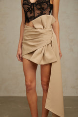 Young woman wearing a beige mini skirt with ruched details and a decorative bow accent at the waist