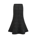 Young woman wearing a black and white checked tweed matching set consisting of a vest top and skirt standing against a plain background