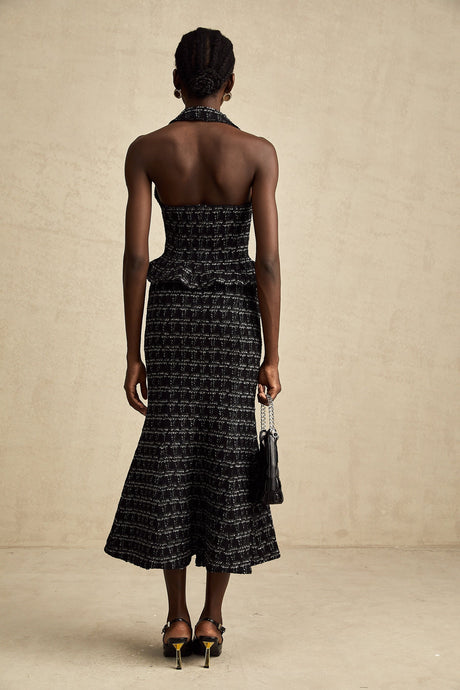 Young woman wearing a black and white checked tweed vest top and matching skirt set against a plain background