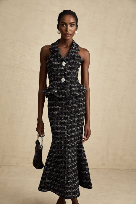 Young woman wearing a black and white checked tweed vest top and matching skirt set against a plain background