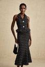 Young woman wearing a black and white checked tweed vest top and matching skirt set against a plain background