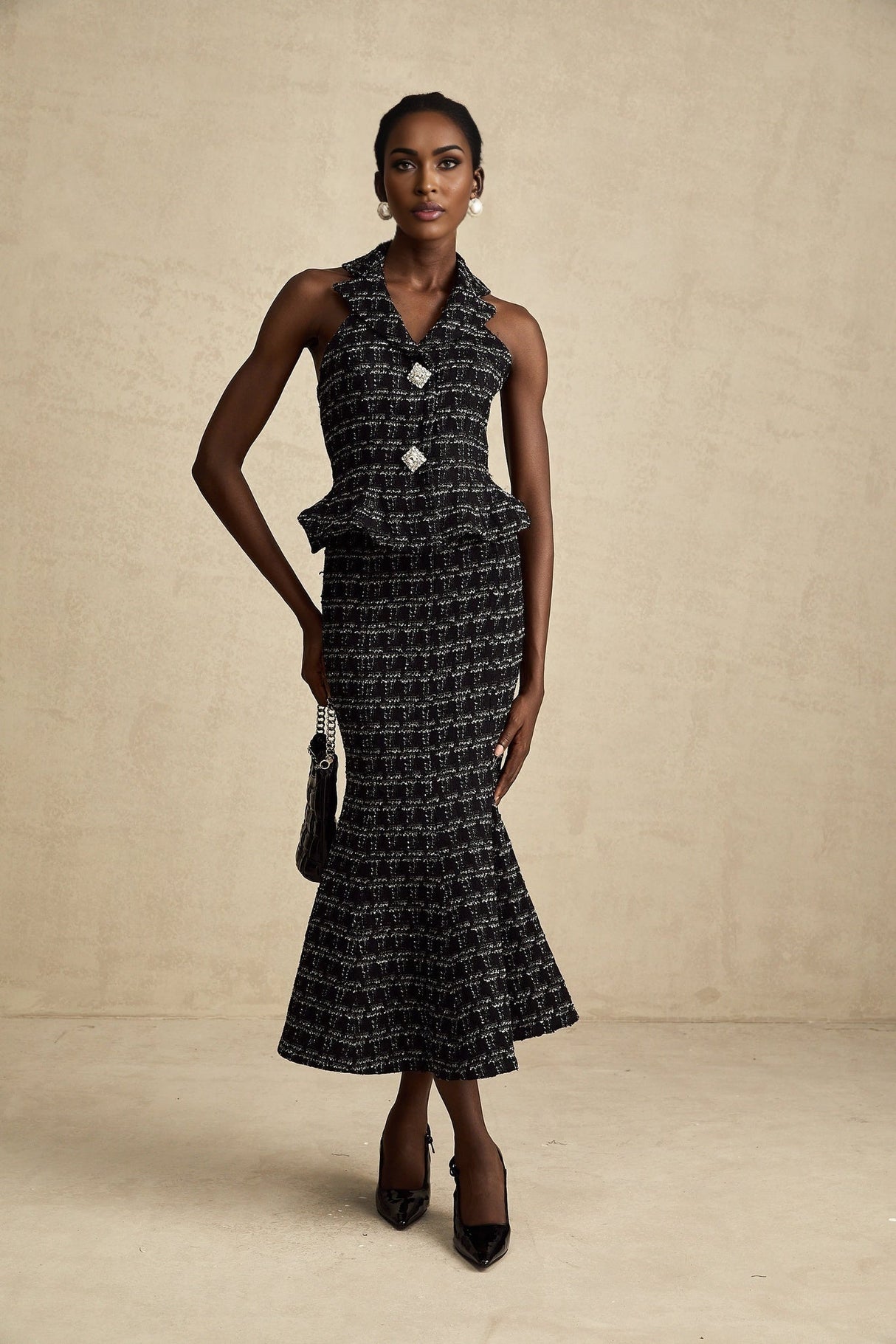 Young woman wearing a black and white checked tweed vest top and matching skirt set standing against a plain background