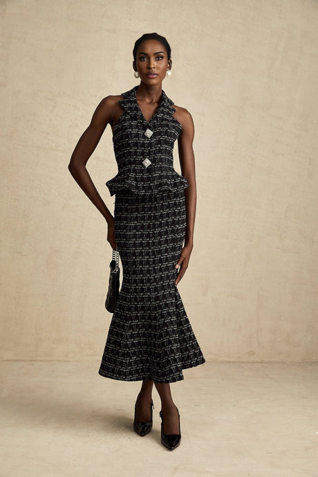 Young woman wearing a black and white checked tweed vest top and matching skirt set standing against a plain background