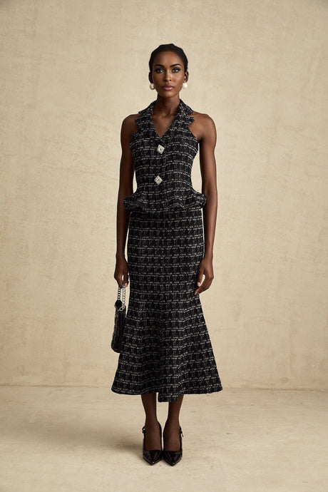 Young woman wearing a black and white checked tweed vest top and matching skirt set standing against a plain background