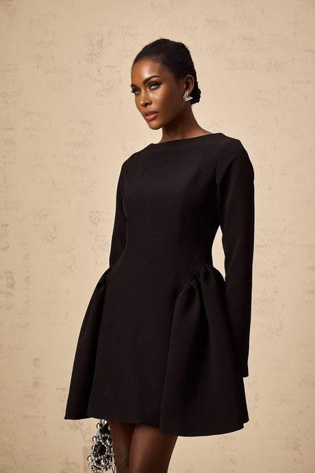 Young woman wearing a black long sleeve mini dress with a flared skirt standing against a plain background