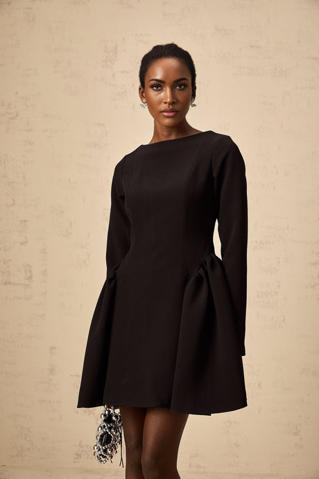 Young woman wearing a black long sleeve mini dress with a flared skirt standing in a neutral background