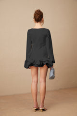 Young woman wearing a black mini dress with a bubble skirt and short sleeves standing against a plain background