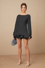 Young woman wearing a black mini dress with a bubble skirt and short sleeves standing against a plain background
