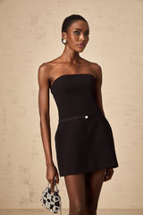 Young woman wearing a black mini dress with puff sleeves and a large bow detail at the neckline