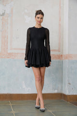 Young woman wearing a black mini dress with puff sleeves and pointelle detailing standing against a plain background