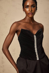 Young woman wearing a black mini dress with ruched detailing and puff sleeves standing against a plain background