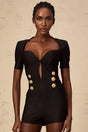 Young woman wearing a black short playsuit with embossed buttons named Solene