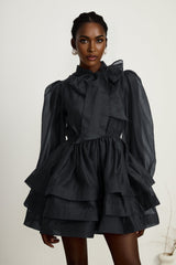 Young woman wearing a black tiered flared mini dress with short sleeves standing against a plain background