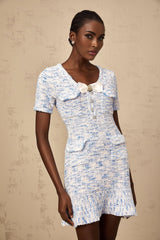 Young woman wearing a blue and white checked knit mini dress with short sleeves and a fitted silhouette standing against a plain background