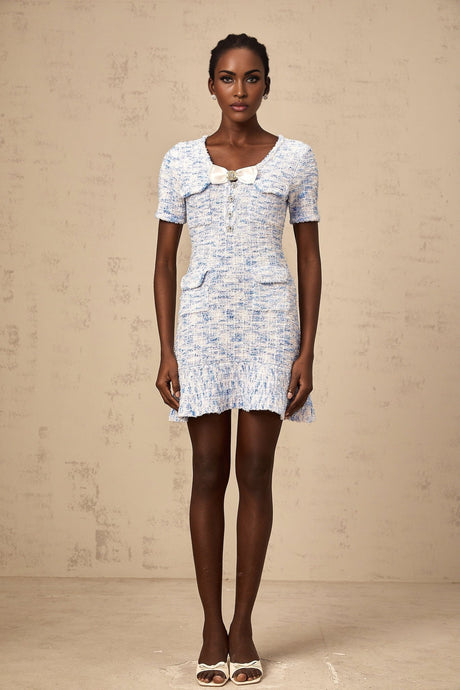 Young woman wearing a blue checked knit mini dress with short sleeves and a fitted silhouette standing against a plain background