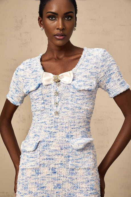 Young woman wearing a blue checked knit mini dress with short sleeves and a fitted silhouette standing against a plain background