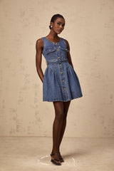 Young woman wearing a blue denim mini dress with a belt cinching the waist standing in a casual pose against a plain background