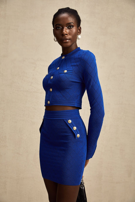 Young woman wearing a blue knitted matching set consisting of a long sleeve top with button details and a fitted skirt