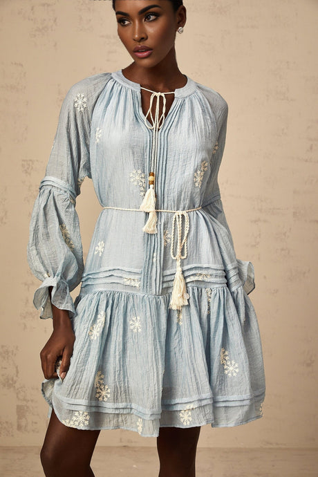 Young woman wearing a blue mini dress with floral embroidery details standing in a casual pose