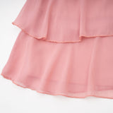 Young woman wearing a briar pink mini dress with tiered skirt and halter neckline standing against plain background