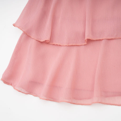 Young woman wearing a briar pink mini dress with tiered skirt and halter neckline standing against plain background