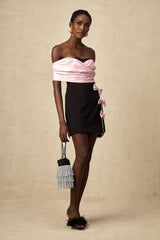 Young woman wearing a colorblocked mini dress with a bow embellishment standing in front of a plain background