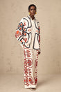 Young woman wearing a colorful floral print matching set consisting of a shirt and trousers standing in a relaxed pose against a plain background
