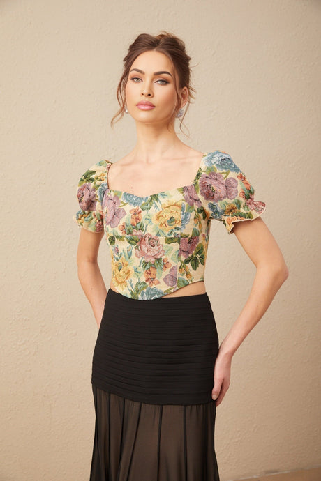 Young woman wearing a cropped floral print top with short puffed sleeves and a square neckline in vibrant colors against a plain background