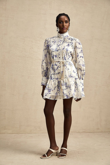 Young woman wearing a floral print chiffon mini dress with flared skirt and short sleeves against a plain background