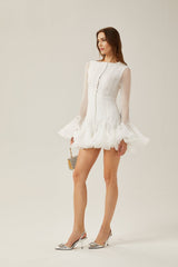 Young woman wearing a flowy light colored semi sheer mini dress with flared short sleeves and a flared skirt standing in front of a plain background
