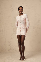 Young woman wearing a formfitting pink knit mini dress with short sleeves standing against a plain background