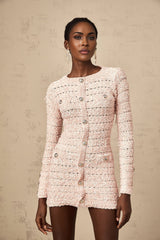 Young woman wearing a formfitting pink mini dress with long sleeves and a high neckline standing against a plain background