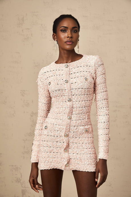 Young woman wearing a formfitting pink mini dress with long sleeves and a high neckline standing against a plain background