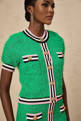 Young woman wearing a green knitted crop top and matching midi skirt set standing against a plain background