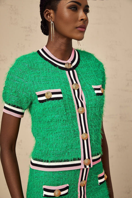 Young woman wearing a green knitted crop top and matching midi skirt set standing against a plain background