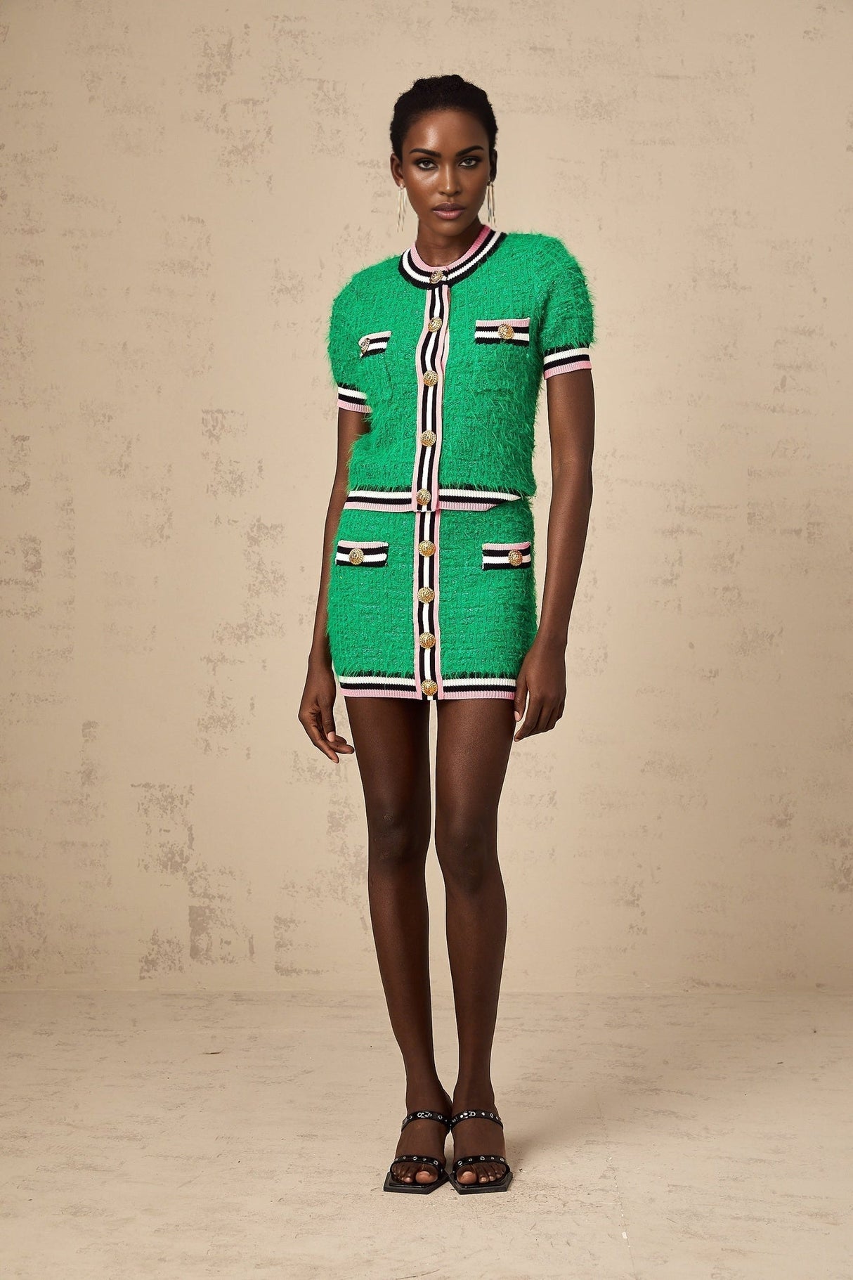 Young woman wearing a green knitted top and matching skirt set standing against a plain background